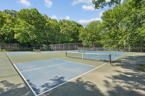 A tennis court surrounded by trees and fencing.