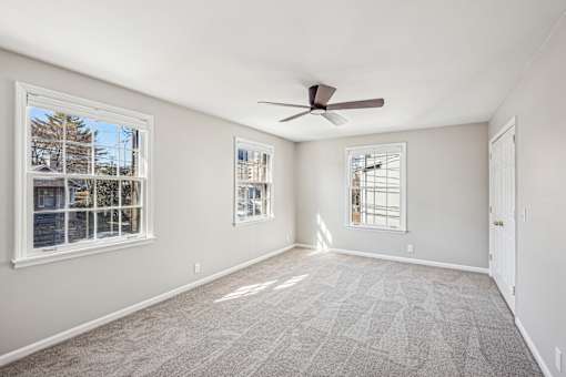A room with a ceiling fan and three windows.