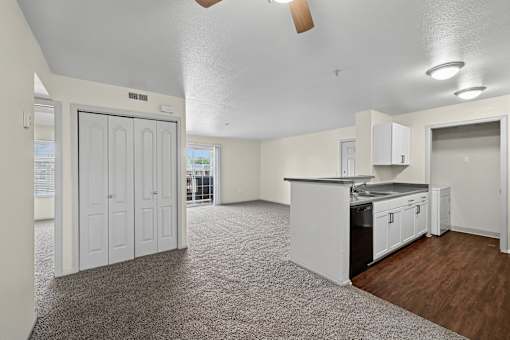 A spacious kitchen and living room with white cabinetry and a grey carpet.