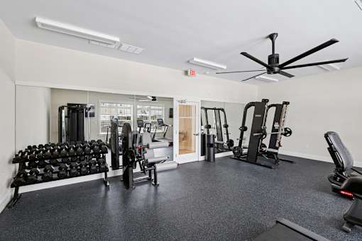 A spacious gym with a variety of equipment including dumbbells, weight machines, and a bench press.