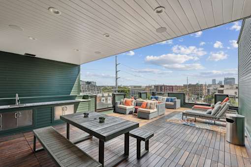 A wooden table and chairs are set up on a wooden deck with a city skyline in the background.