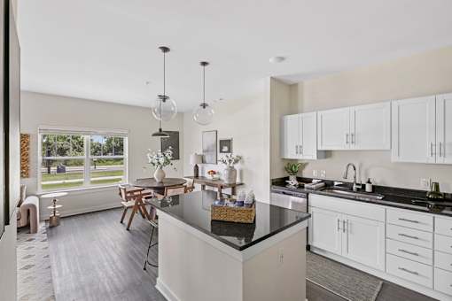 A kitchen with a black countertop and white cabinets and dining room..