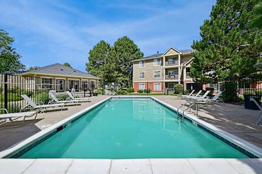 A swimming pool in front of a building with a fence and trees in the background.