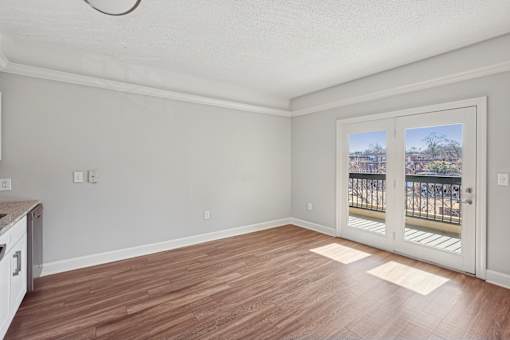 A room with wooden flooring and a view of a balcony through the sliding glass door.