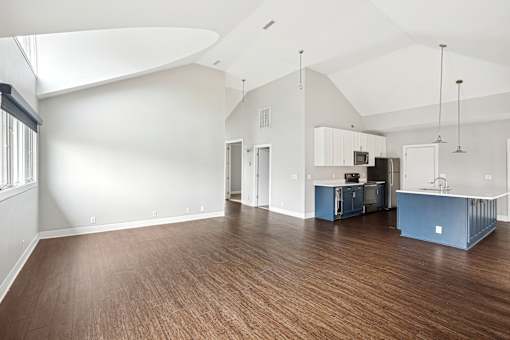 A spacious room with wooden floors and a kitchen area with white cabinets.