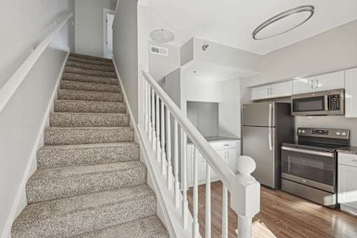 A staircase with a carpeted runner and white balusters leads to a kitchen with stainless steel appliances.
