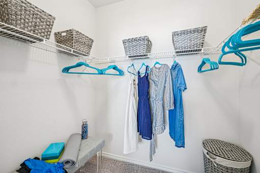 A white closet with clothes hanging and baskets on the shelf.