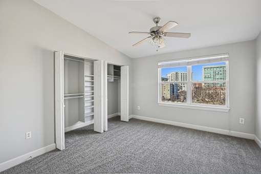 A room with a ceiling fan and a window overlooking a cityscape.