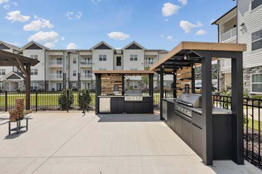 A sunny day at a residential complex with a covered walkway and apartment buildings with outdoor kitchen and grills.