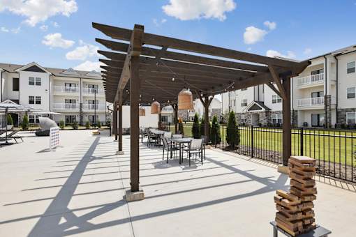 A pool sundeck with a table and chairs under a wooden pergola.