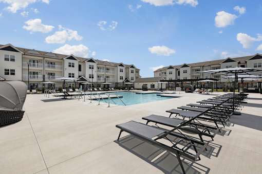 A sunny day at the poolside with lounge chairs and apartment buildings in the background.