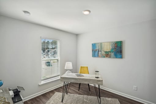 an office with white walls and a window with white blinds and a table with