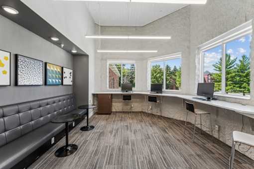 A room with a grey couch, a table, and a window with a view of trees and a building outside.
