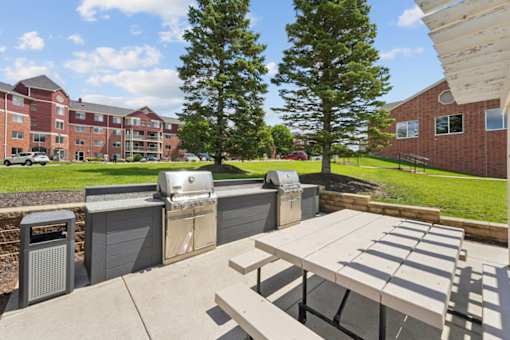 A picnic table is in the middle of a courtyard with a tree and a building in the background.