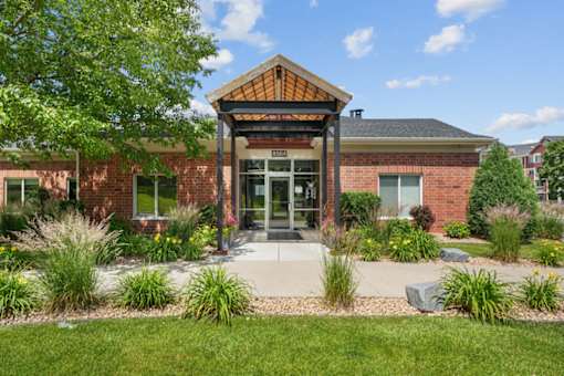 A building with a brick facade and a glass door is surrounded by greenery.