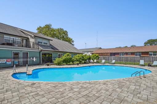 A swimming pool surrounded by a brick patio and apartment buildings.
