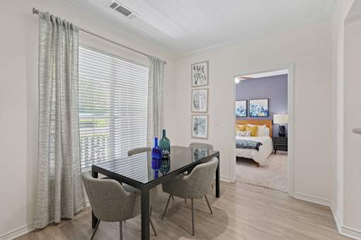 A dining room with a table and chairs and a view of a bedroom through the window.
