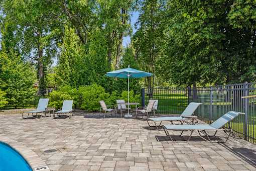 A poolside area with a blue umbrella and several lounge chairs.