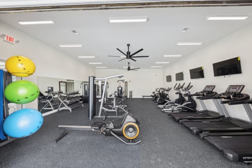 a gym with cardio machines and weights and a ceiling fan