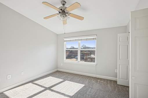 A room with a ceiling fan and a window overlooking a cityscape.