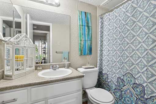 A bathroom with a white toilet, sink, and a birdcage on the counter.