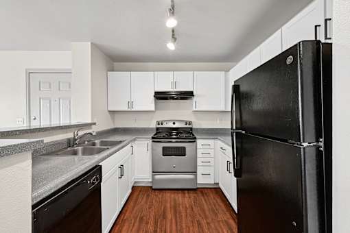 A black refrigerator stands in a kitchen with white cabinets and a stove.