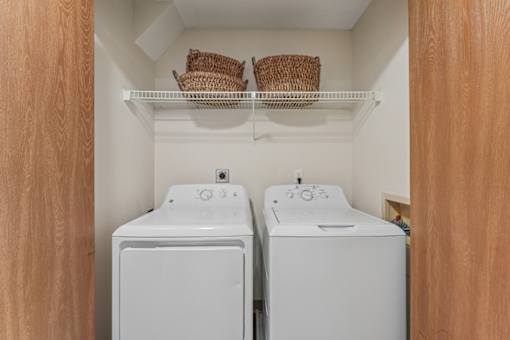 A laundry room with two washing machines and baskets on the shelf.