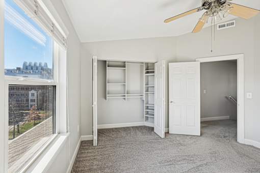 A room with a window, a fan, and a view of a city skyline.