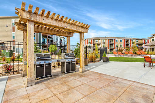 A wooden pergola is in front of two grills and a fence.