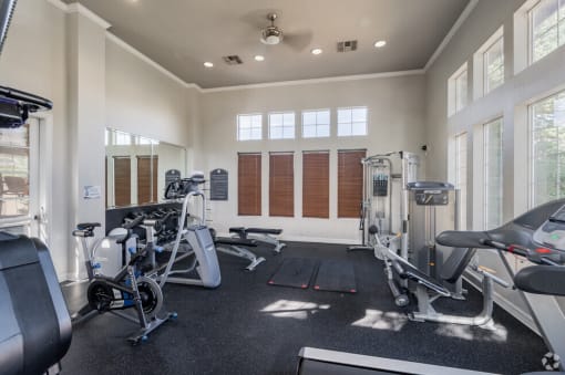 Aurora, CO, Apartments for Rent - Sonoma Resort at Saddle Rock - Fitness Center with Cardio Machines, Strength Training Equipment, Ceiling Fan, Mirrors, and Windows.