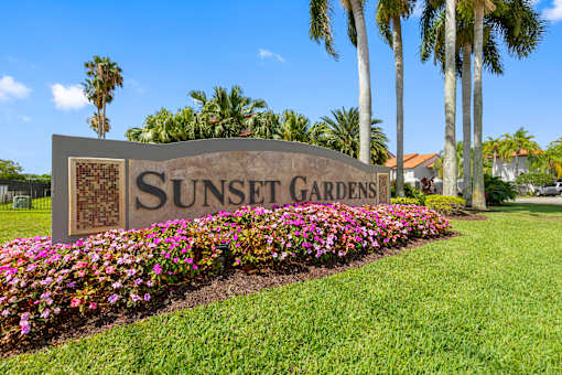A sign that says Sunset Gardens in front of some flowers.