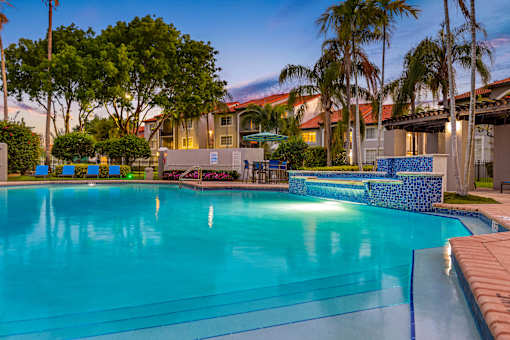 A swimming pool surrounded by palm trees and a building in the background.