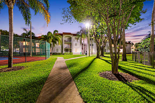 A pathway leads through a grassy area with trees and a tennis court.
