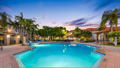 A large swimming pool surrounded by palm trees and a building in the background.