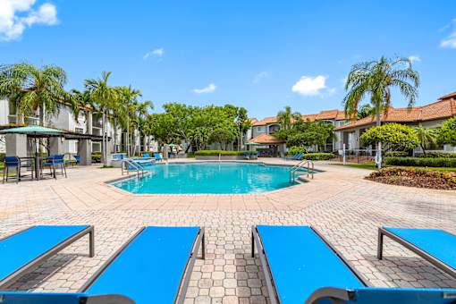 A swimming pool surrounded by blue lounge chairs and palm trees.