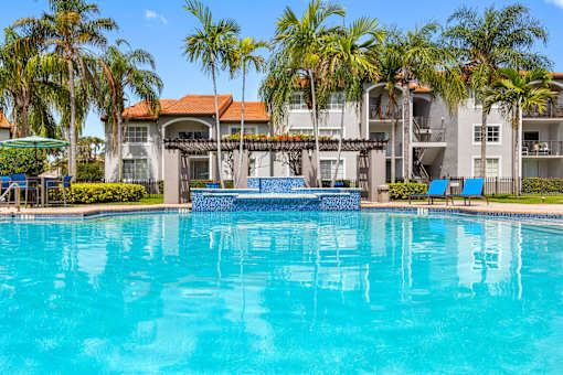 A swimming pool surrounded by palm trees and a building in the background.