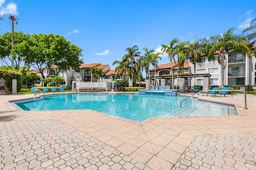 A large swimming pool surrounded by a brick patio and palm trees.