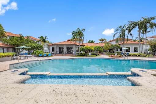 A large swimming pool surrounded by a concrete patio and palm trees.