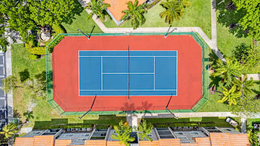 A tennis court is surrounded by trees and buildings.