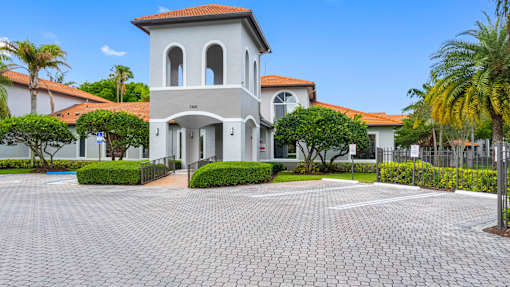 A white building with a red roof and a grey tiled courtyard in front.
