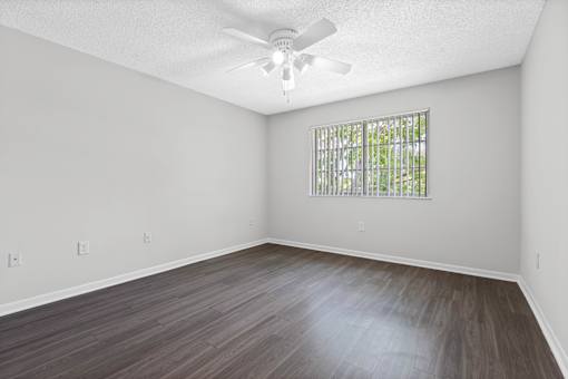 A room with a ceiling fan and a window with bars.