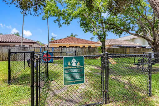 A sign welcoming visitors to a dog park is displayed on a fence.