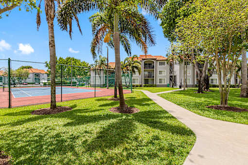 A tennis court is surrounded by a green fence and trees.