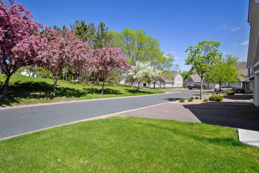 Seasons Villas - Exterior View of Driveway With Lush Grass, Trees, and a View of the Street