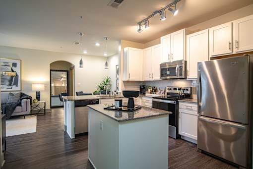 Two-Bedroom Apartments in West Nashville, TN - The Summit at Nashville West - Kitchen with White Cabinets, Granite Island, Track Lighting, and Stainless Steel Appliances Over Wood Look Flooring.