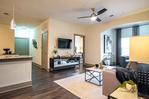 A modern living room with a flat screen TV and a kitchen area in the background.