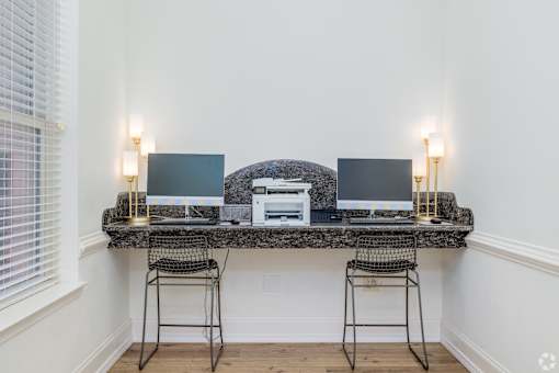 Two laptops are on a desk with a chair on either side.