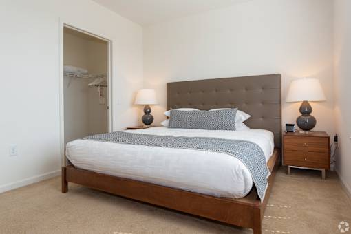 A bedroom with a large bed and two lamps on the nightstand.