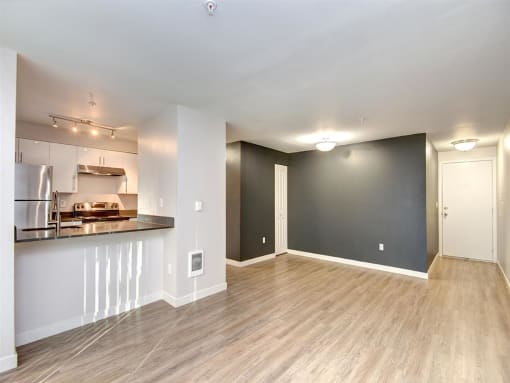 an empty living room with a kitchen in the background