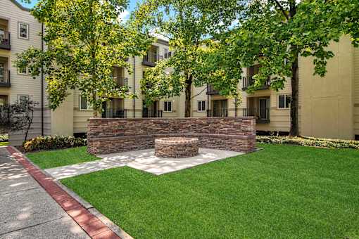 A small garden with a stone wall and a bench in front of apartment buildings.